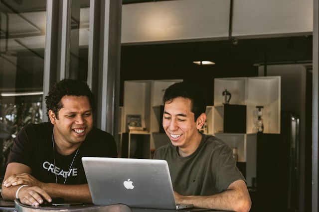 Two people seated at a desk, looking at a laptop in a modern office environment.